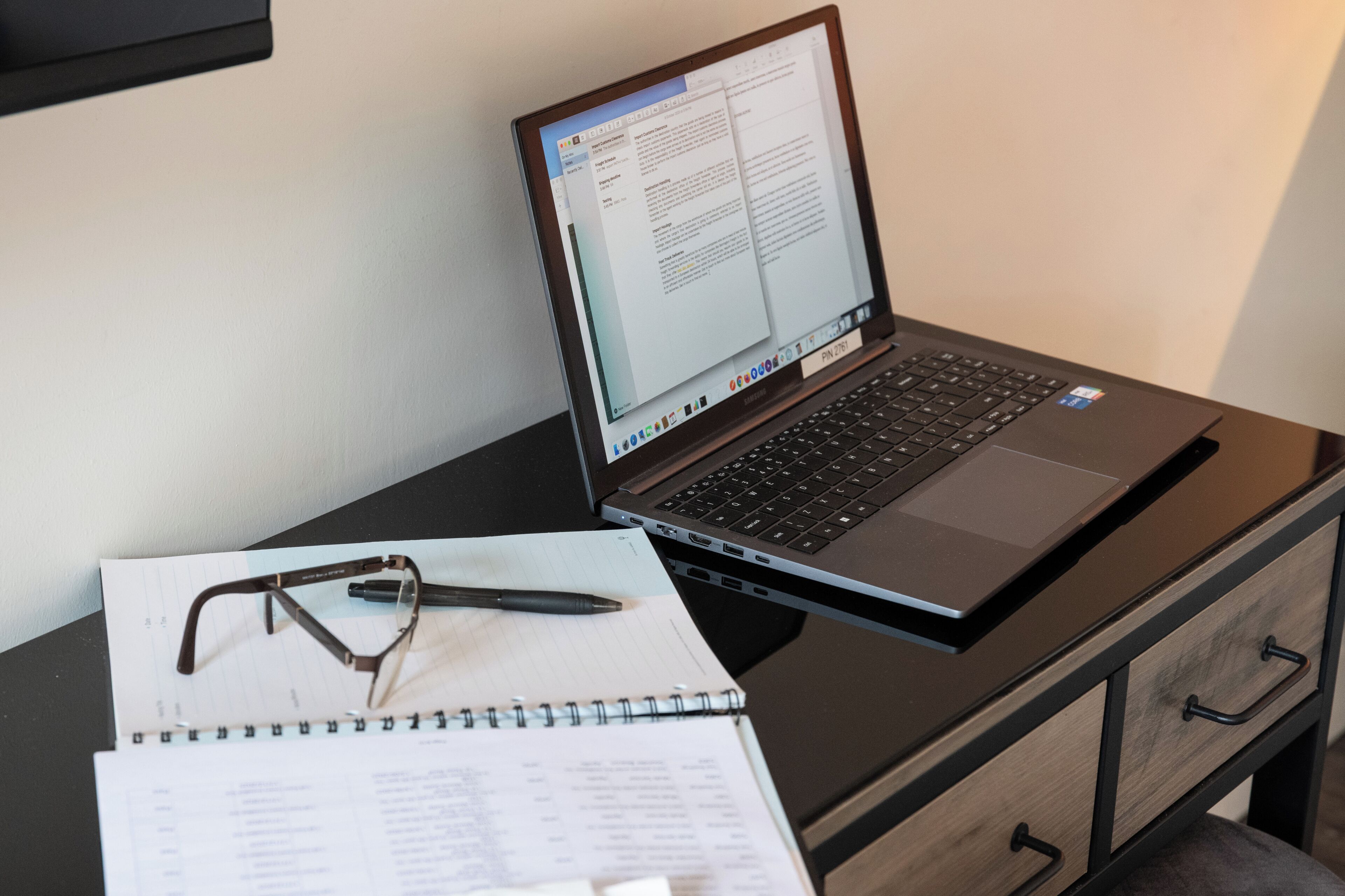 A laptop on a desk with a notebook and glasses.
