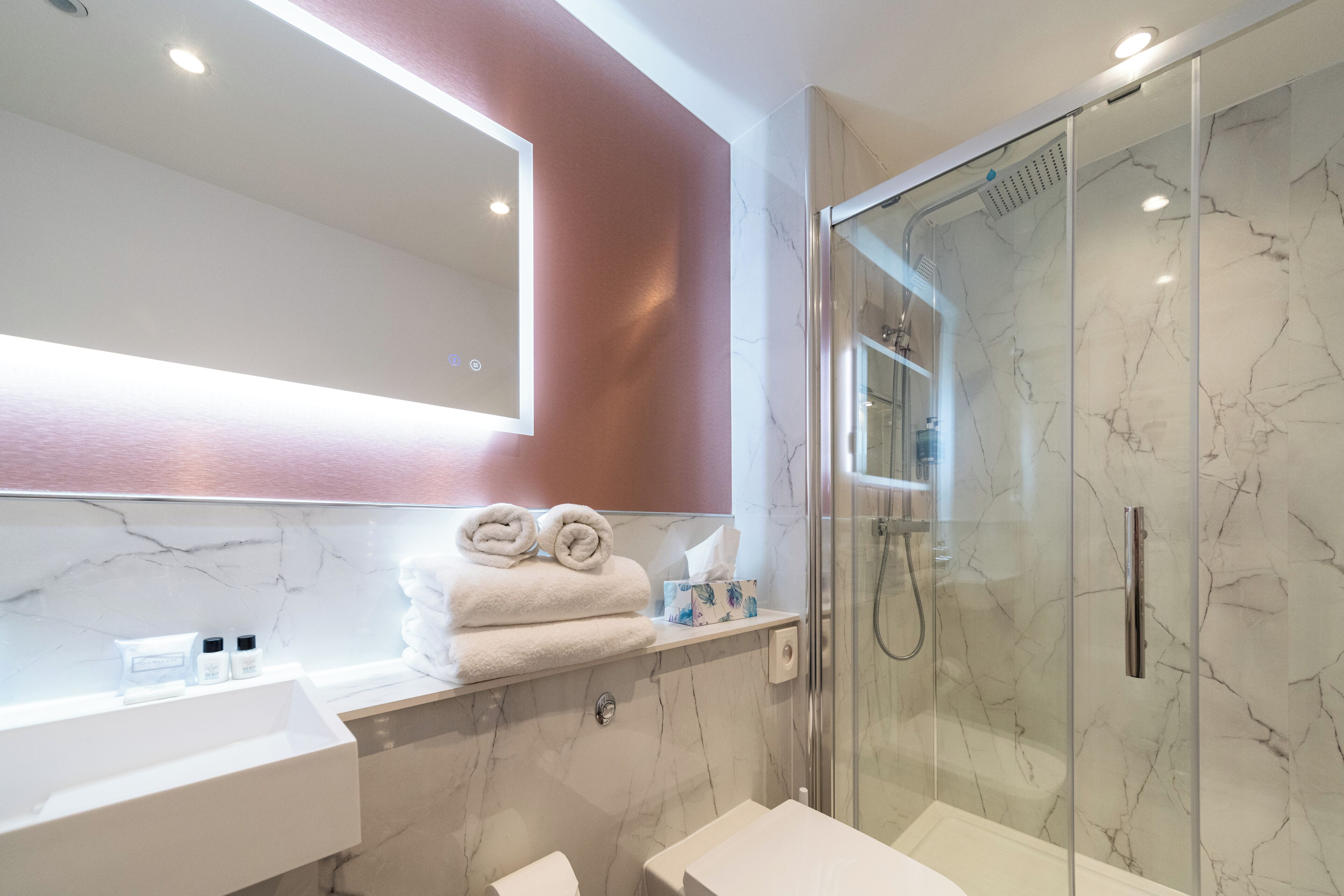 A modern bathroom with a glass-enclosed shower, a white sink, and a marble backsplash.