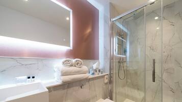 A modern bathroom with a glass-enclosed shower, a white sink, and a marble backsplash.