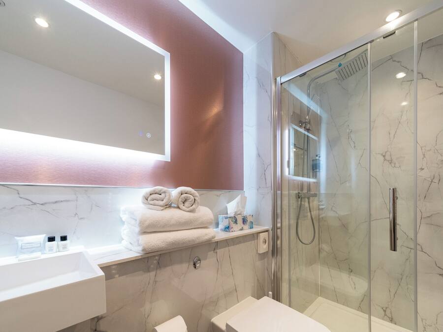 A modern bathroom with a glass-enclosed shower, a white sink, and a marble backsplash.