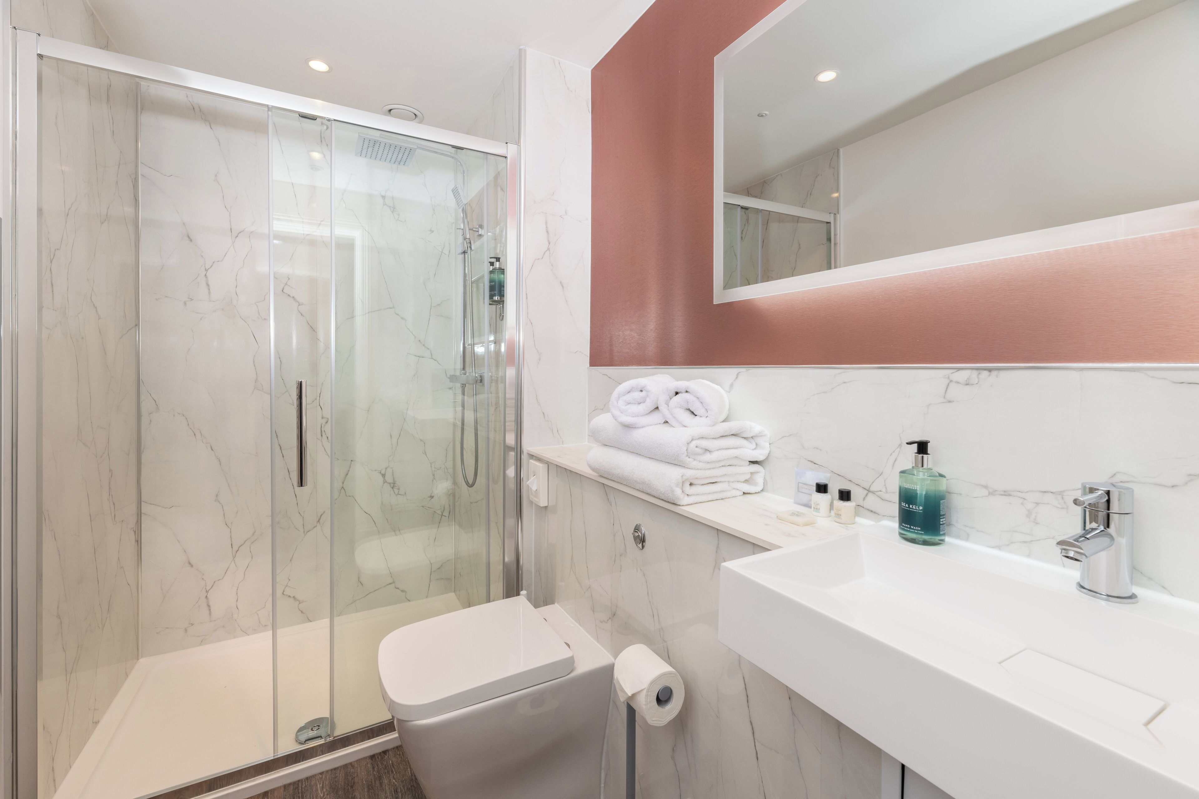 Un baño moderno con ducha envuelta en vidrio, un lavamanos blanco y un espejo sobre el mueble.