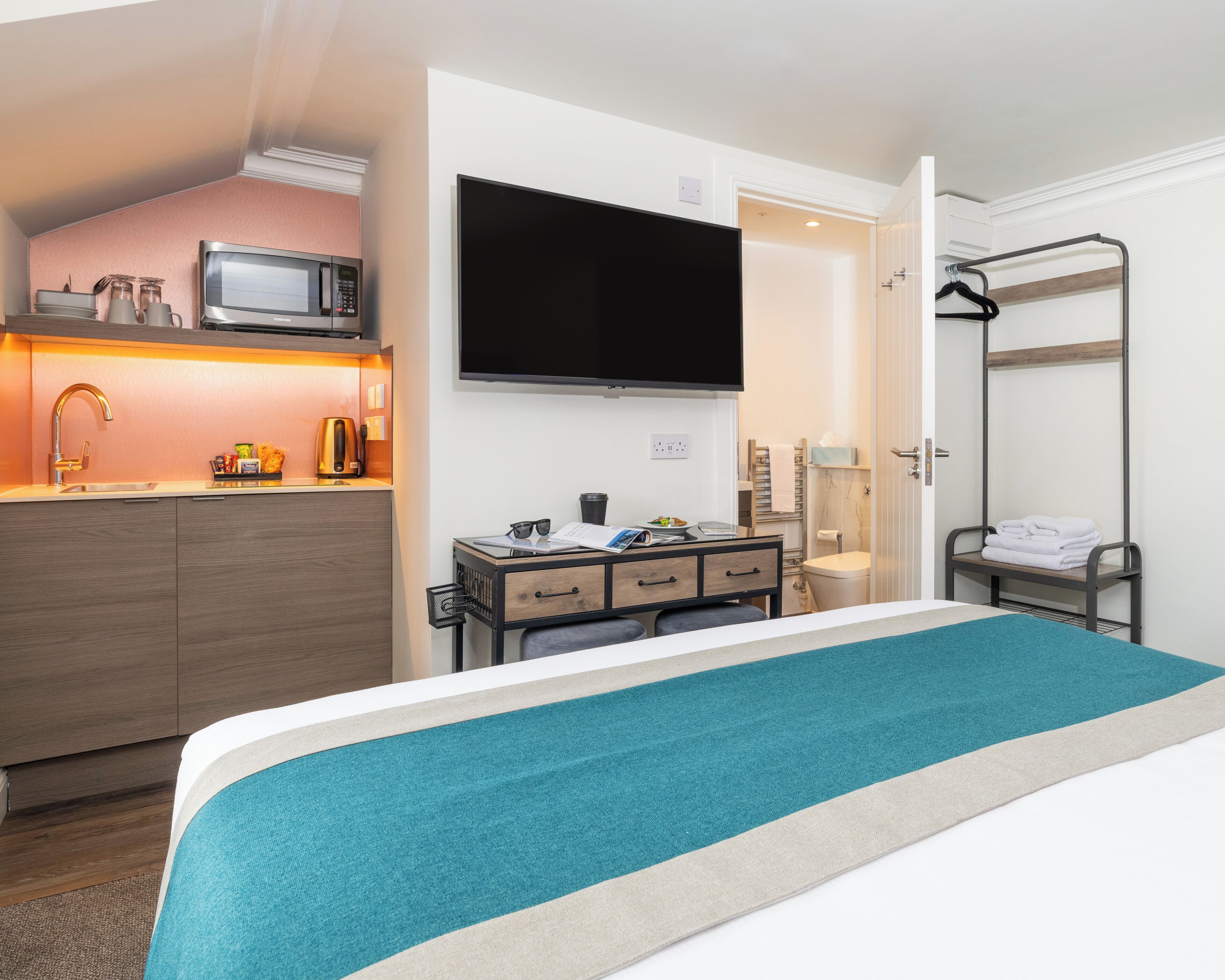 A hotel room with a bed, a desk with a flat-screen TV, a microwave, a sink, and a shower area.