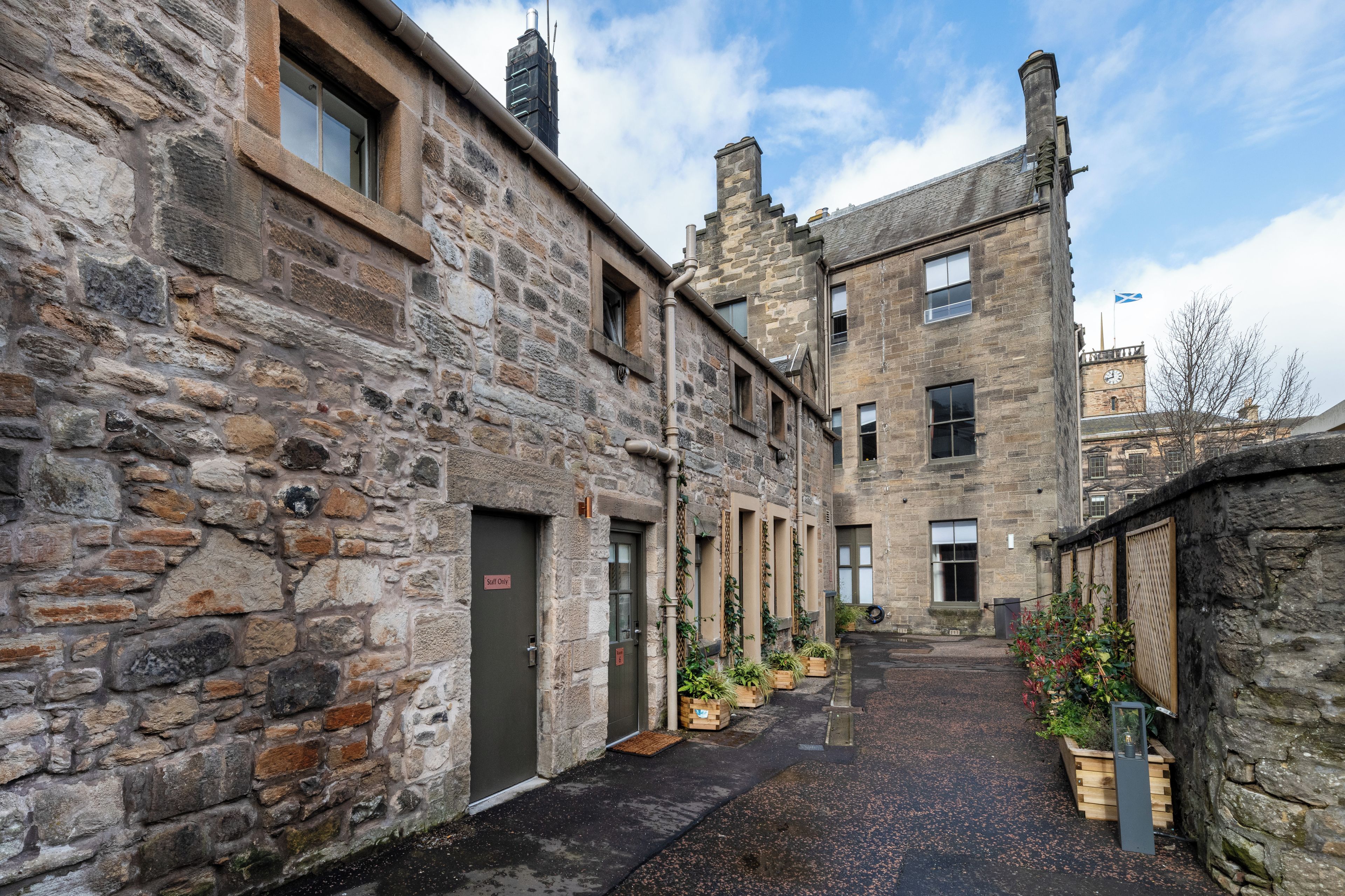 A narrow alleyway between stone buildings with a traditional clock tower in the background.