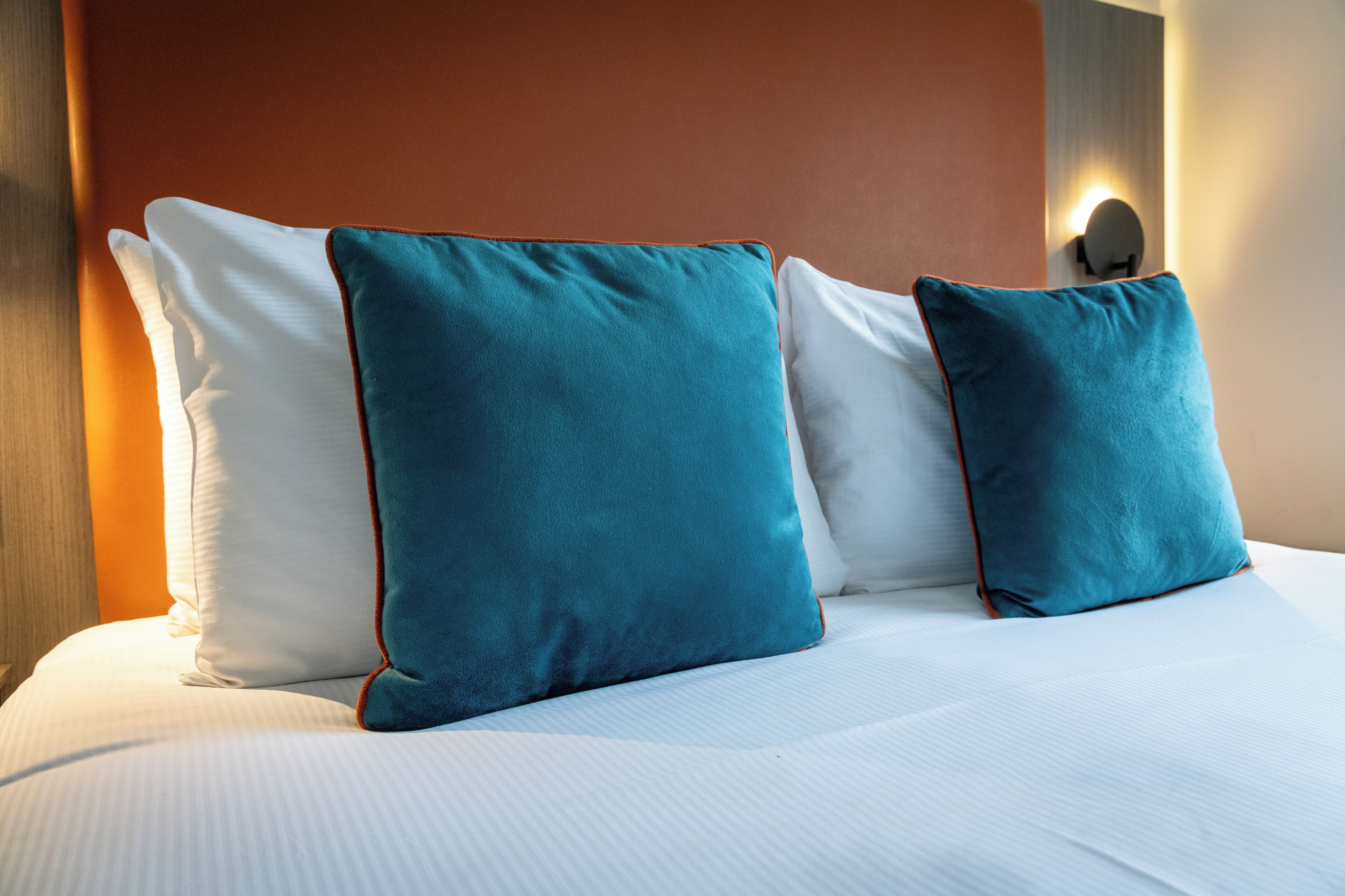 A neatly made bed with white linens and two teal pillows.