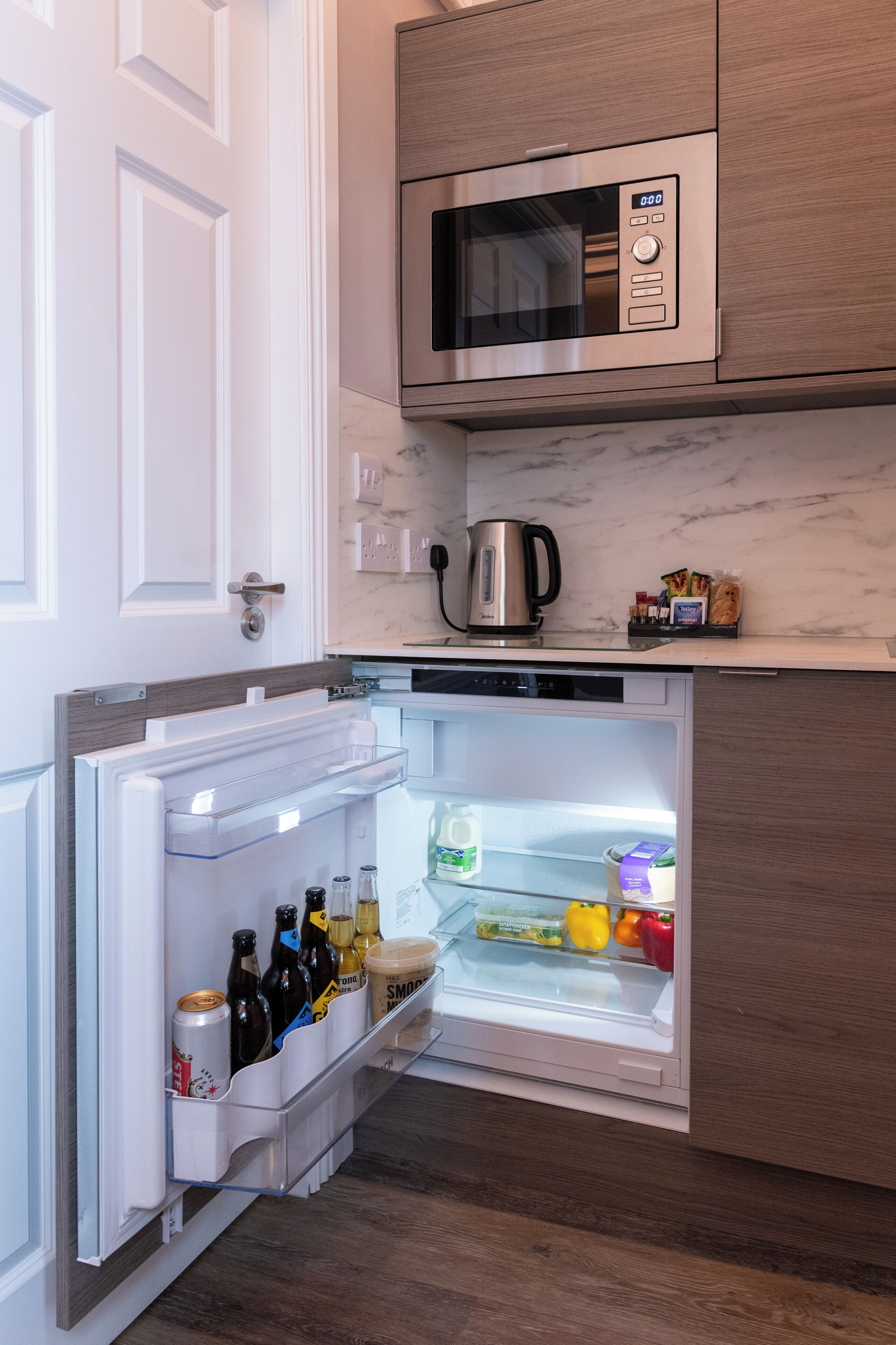 Una cuina compacta amb microones integrat, nevera amb refrigerador de vi i cafetera a la superfície.