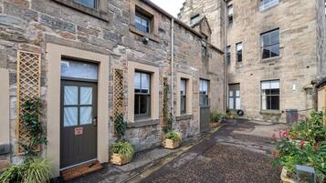 A stone building with multiple windows and doors, some with curtains, and a small garden area with potted plants.