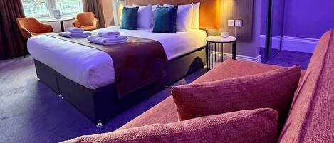 Hotelkamer met een bed, een zithoek met stoelen, een raam met gordijnen en uitzicht op een gebouw.