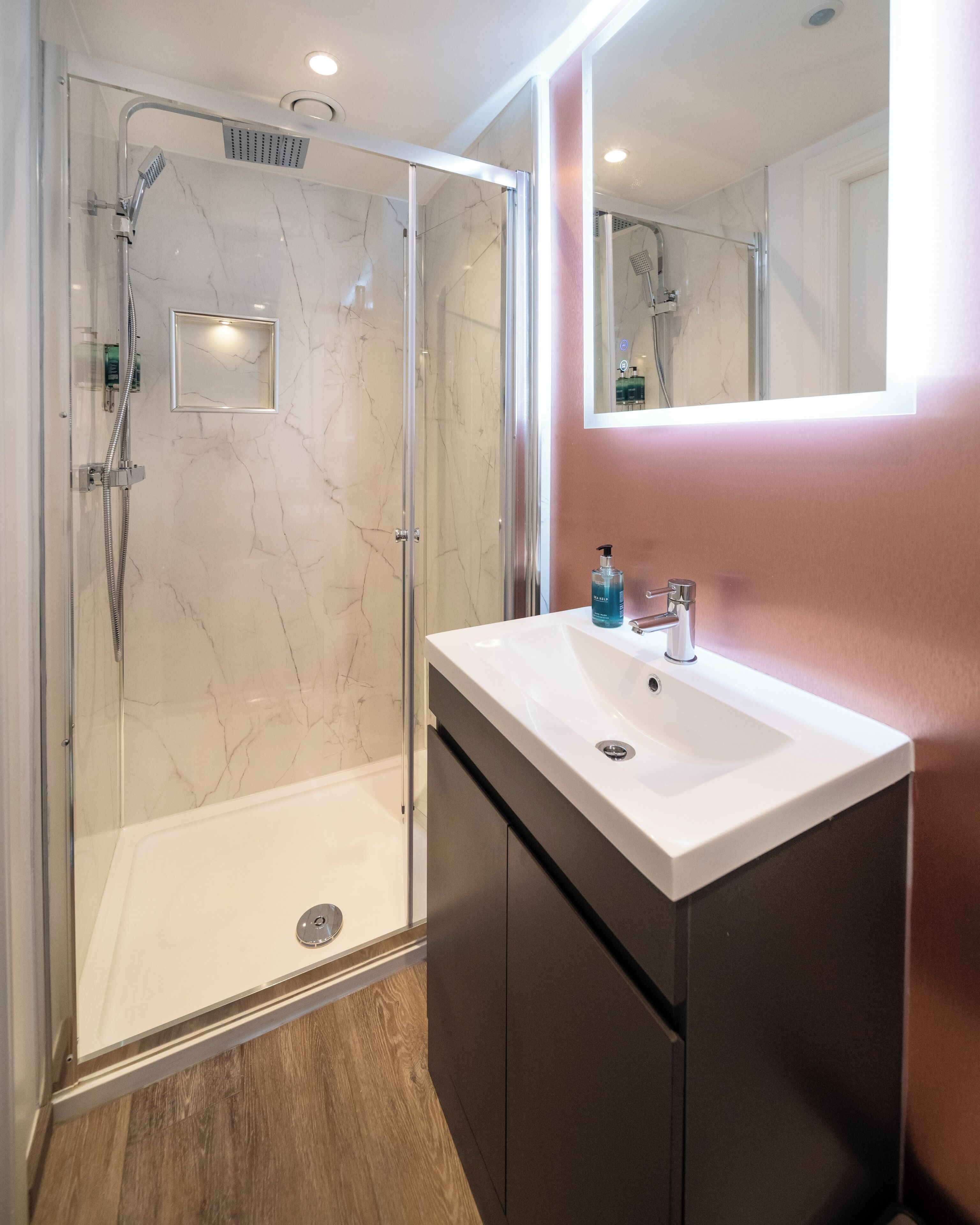 Un baño moderno con ducha de vidrio, un lavamanos blanco y un espejo encima.