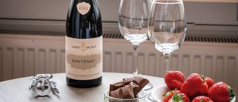A bottle of wine, two glasses, and a bowl of strawberries on a table with a sign in the background.