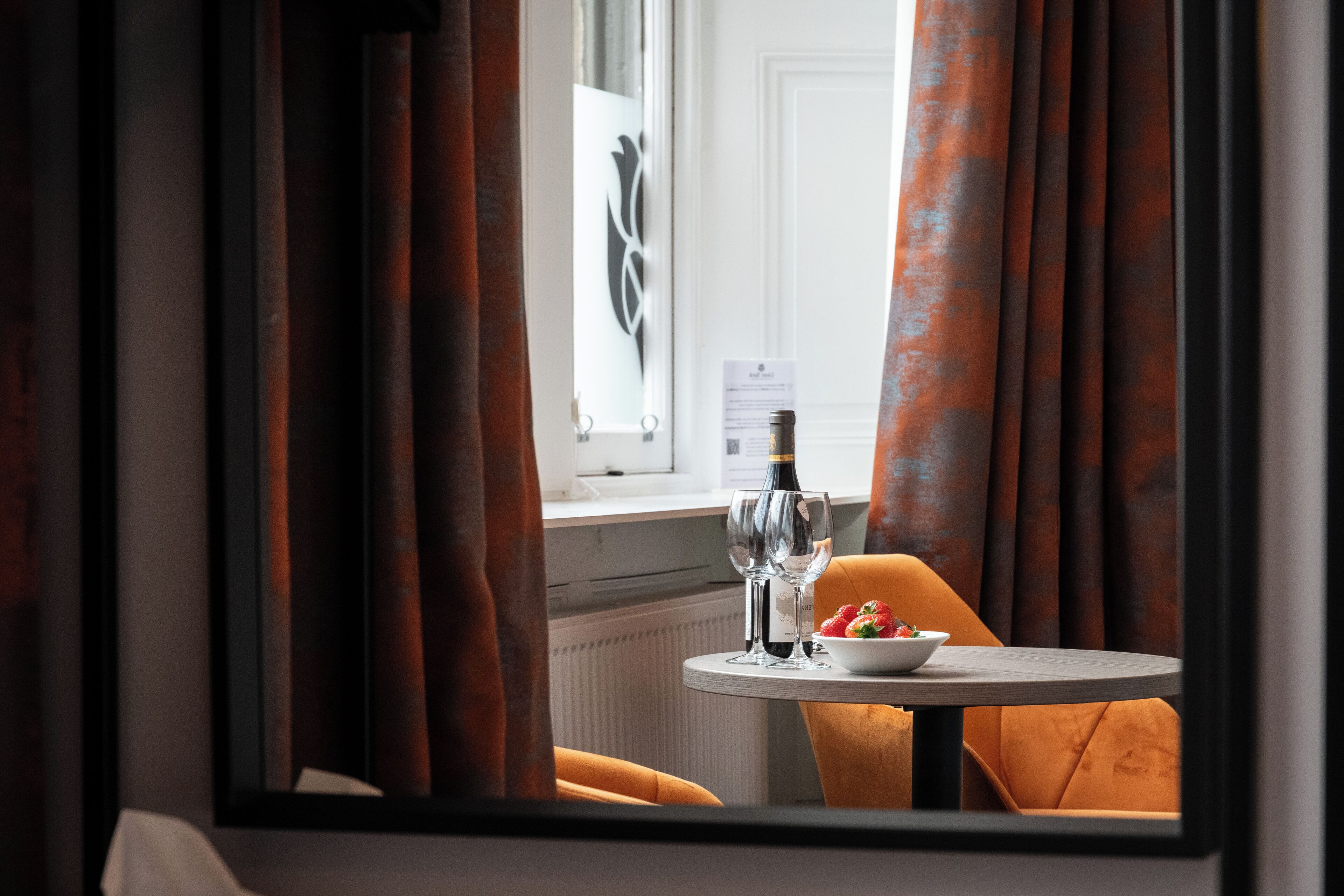Habitación de hotel con vista por la ventana, una mesa con un frutero y copas de vino, y una silla.