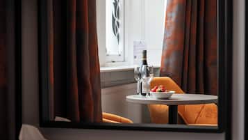 Habitación de hotel con vista por la ventana, una mesa con un frutero y copas de vino, y una silla.