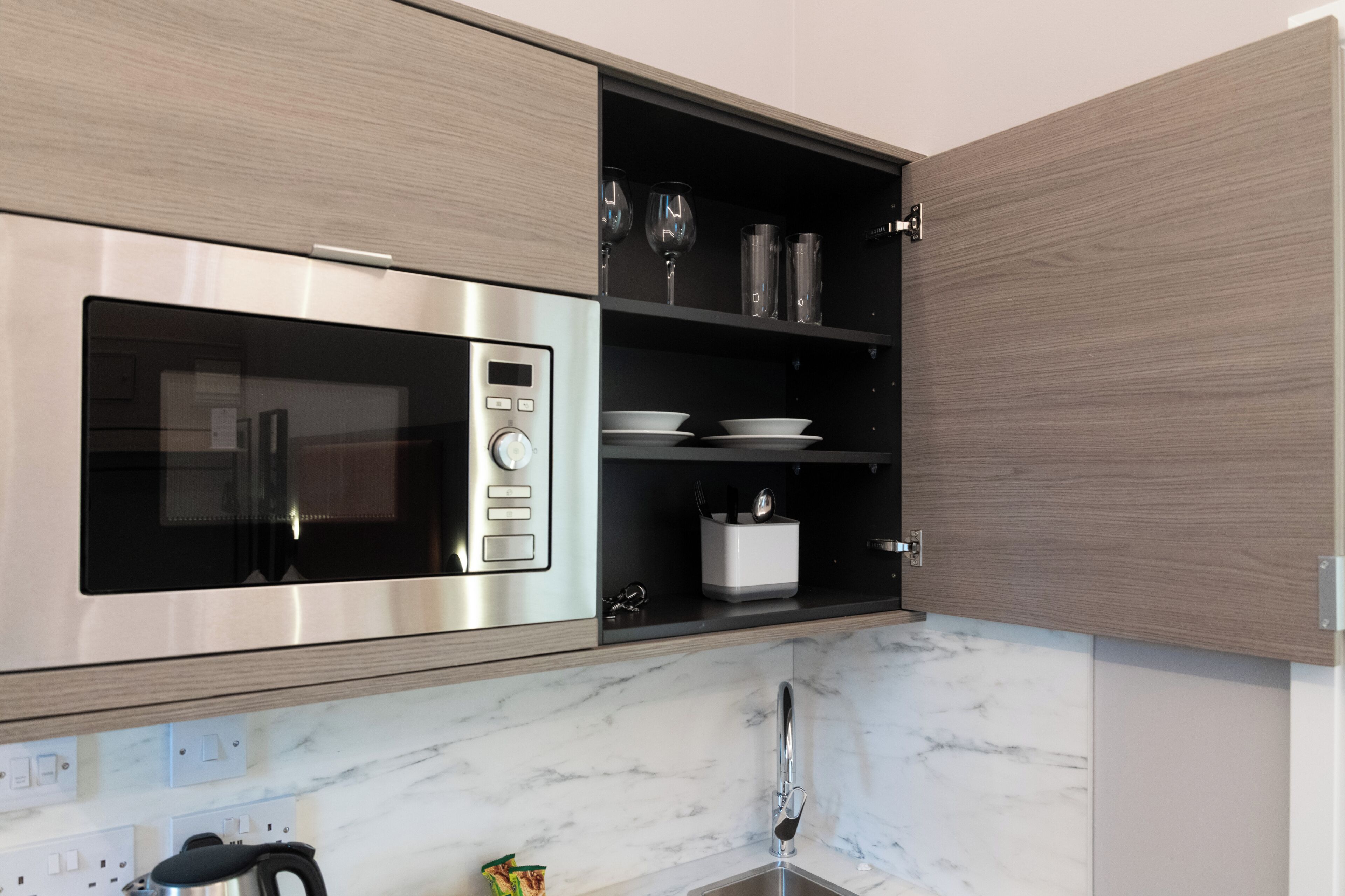 Een moderne keuken met een ingebouwde magnetron, een spoelbak en een wijnrek.