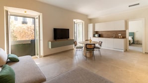 Ein modernes Wohnzimmer mit einer Couch, einem Esstisch mit Stühlen, einem Fernseher und einer Küchenzeile mit Schränken.