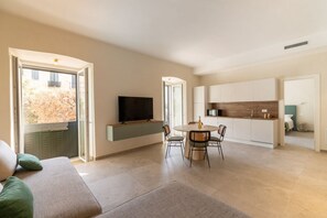 A modern living room with a sofa, a dining table with chairs, a TV, and a kitchen area with cabinets.