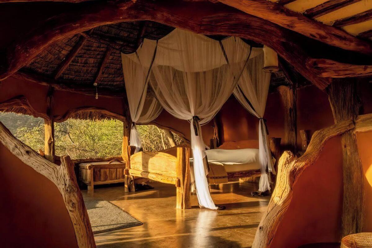 A rustic room with a wooden ceiling, a bed with white curtains, and a bench.