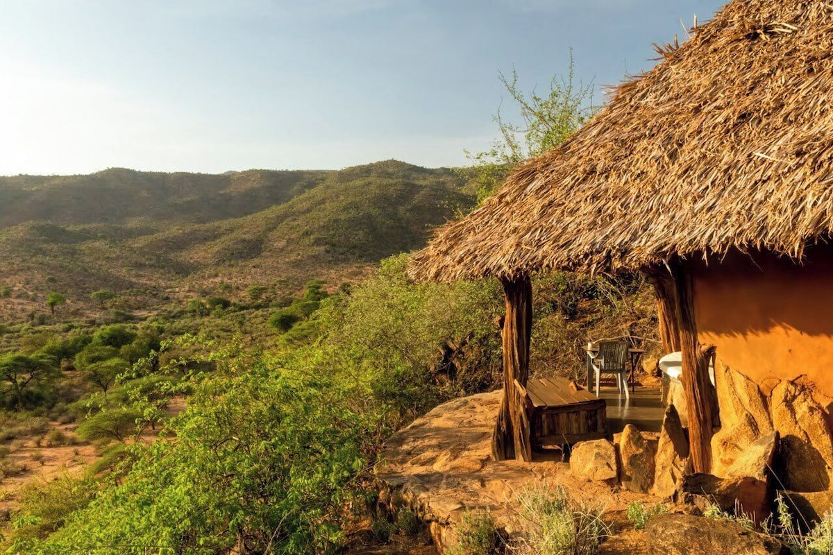 A rustic hut with a thatched roof, surrounded by rocky terrain and sparse vegetation.