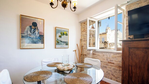 A dining area with a glass table surrounded by white chairs, a chandelier, and artwork on the walls. - Korifo Old Town by Corfu Escapes (Corfu)