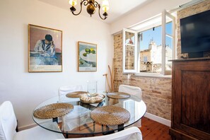 Un coin repas avec une table en verre entourée de chaises blanches, un lustre et des œuvres d’art accrochées aux murs.