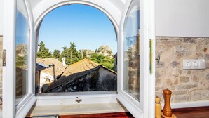 A room with a large arched window offering a view of a hillside with buildings and greenery. - Korifo Old Town by Corfu Escapes (Corfu)