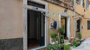 A narrow street with a building featuring a shop with potted plants and a sign reading "GREEK TOOTS". - Korifo Old Town by Corfu Escapes (Corfu)