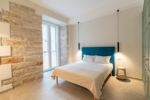 Une chambre avec un mur en pierre, un lit avec une literie blanche et une tête de lit bleue.