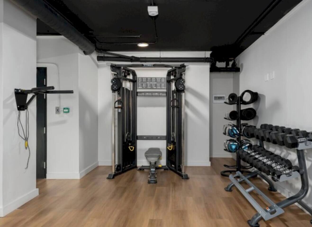 Un gimnasio con una estructura para sentadillas, banca para press de banca y mancuernas.