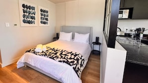 Een moderne hotelkamer met een groot bed, een nachtkastje en een keukenruimte zichtbaar door een geopende deur.