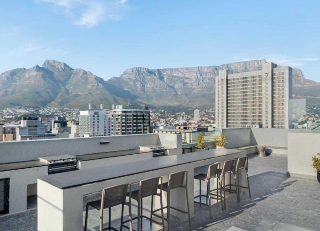Une terrasse sur le toit avec un espace bar, des sièges et une vue panoramique sur la ville, avec des montagnes en arrière-plan.