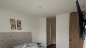 Quarto com cama, televisão fixada na parede e porta que dá para outro cômodo.