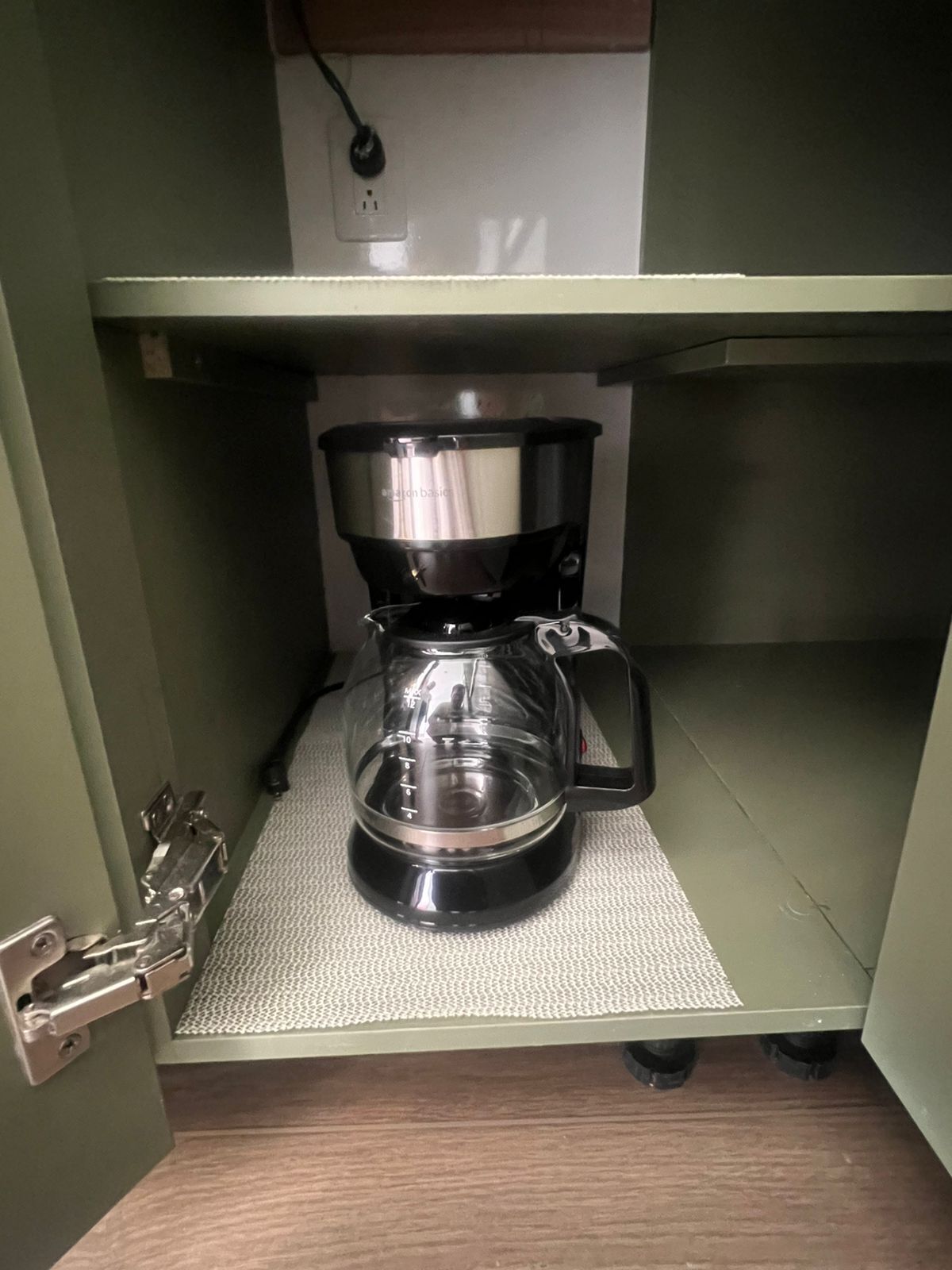 Una cafetera sobre una estantería, con un enchufe encima.