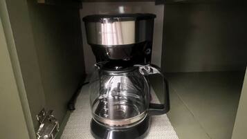 Una cafetera sobre una estantería, con un enchufe encima.