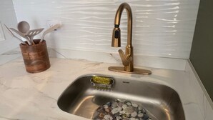 Cozinha com pia de aço inoxidável, suporte de utensílios de madeira e painel de parede com textura.