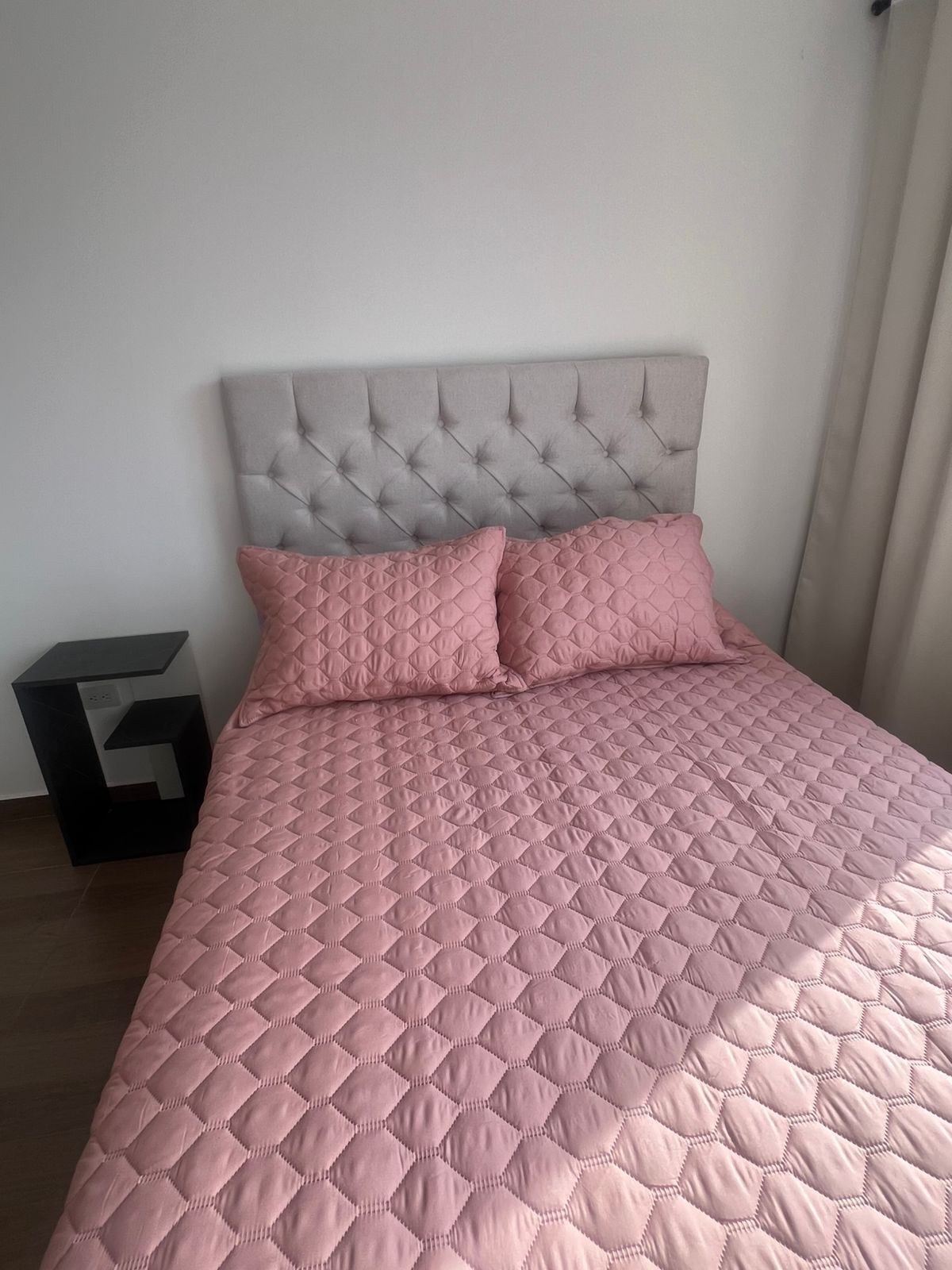 Una cama con cabecera capitonada y ropa de cama rosa acolchada.