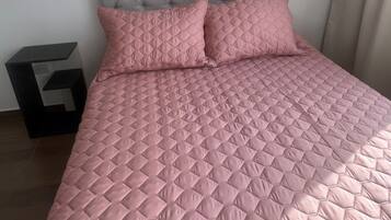 Una cama con cabecera capitonada y ropa de cama rosa acolchada.