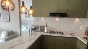 Cozinha moderna com armários verdes, bancada de mármore e iluminação pendente.