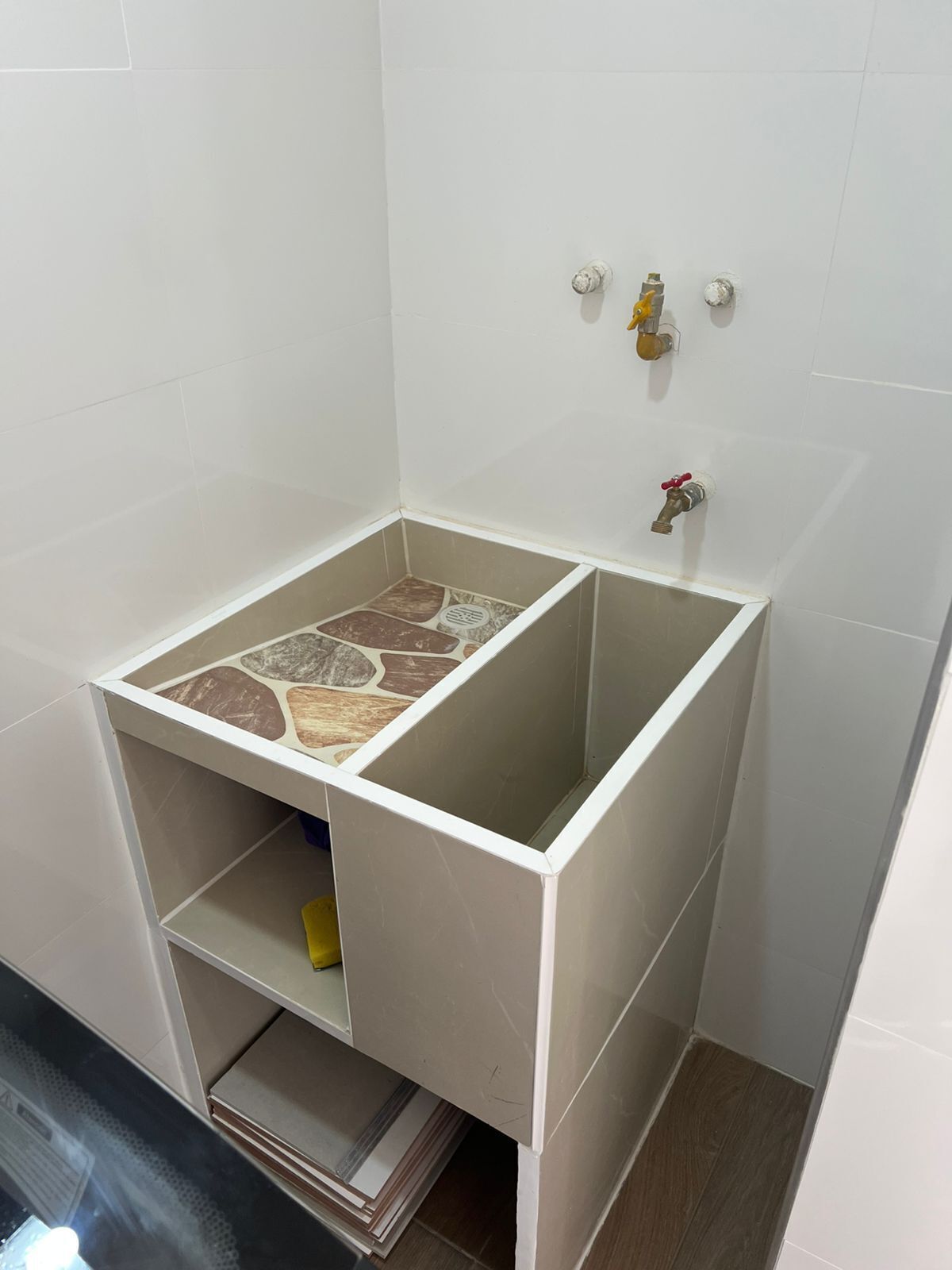 A bathroom with a tiled floor, a white sink, and two faucets.