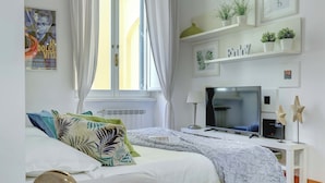 A modern bedroom with a bed, a TV, a desk, and shelves with plants.