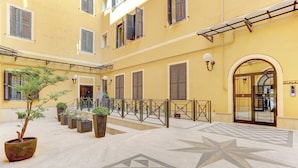 A courtyard with a tiled floor, potted plants, and a staircase leading to an upper level.