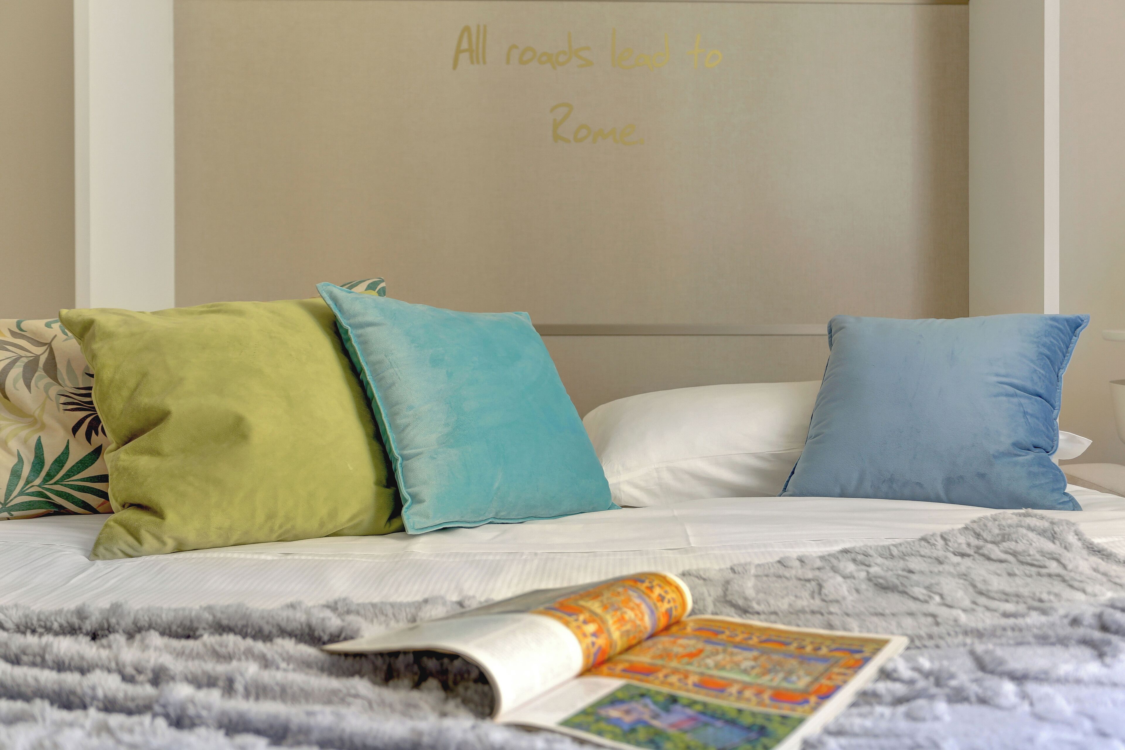 A bed with three pillows, a blanket, and a magazine on a bedspread.