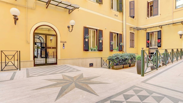 A yellow building with a star-shaped tile pattern on the floor, a large arched entrance, and potted plants on the balcony.