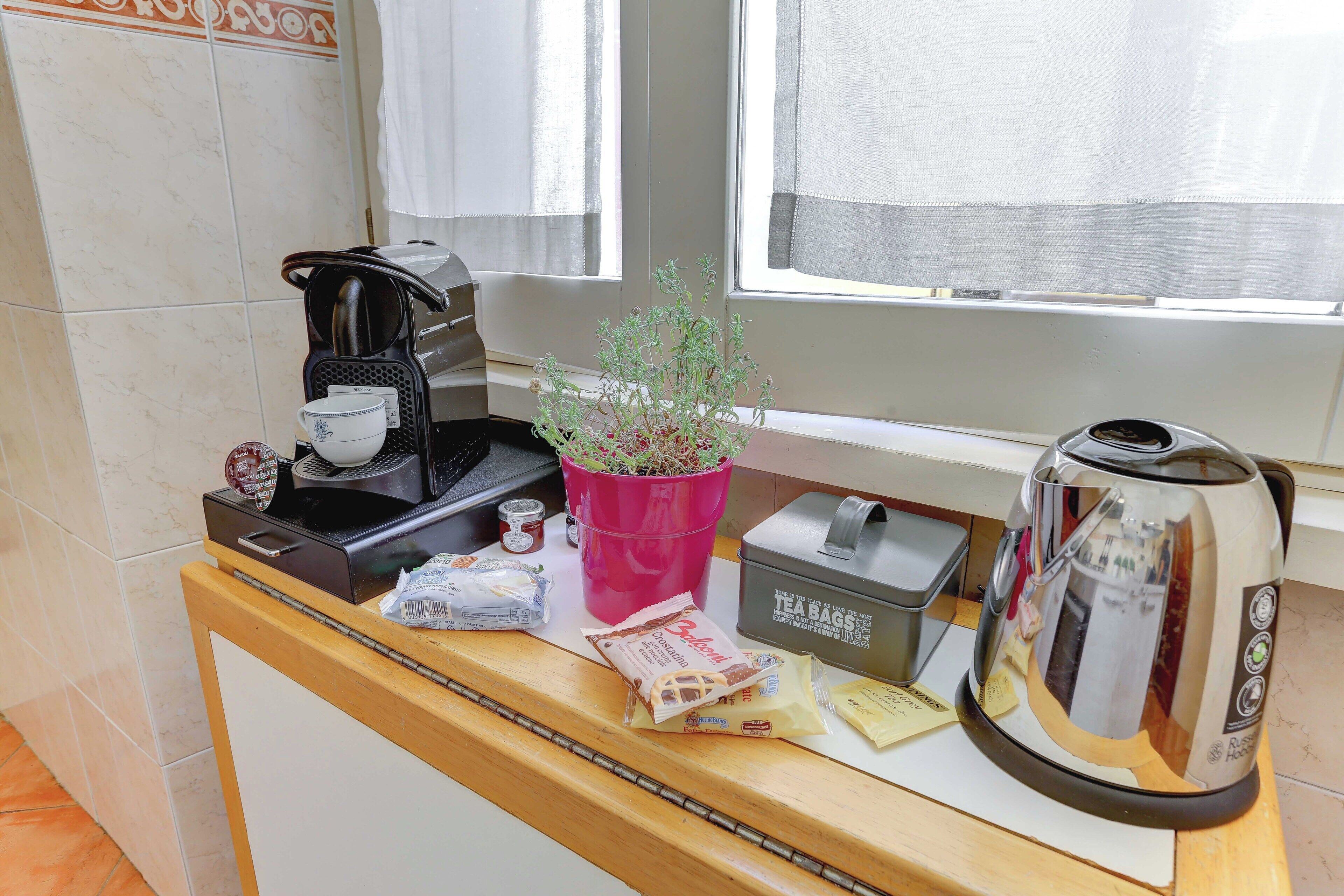 Una encimera de cocina con una cafetera, una planta en maceta, bolsitas de té y un hervidor.