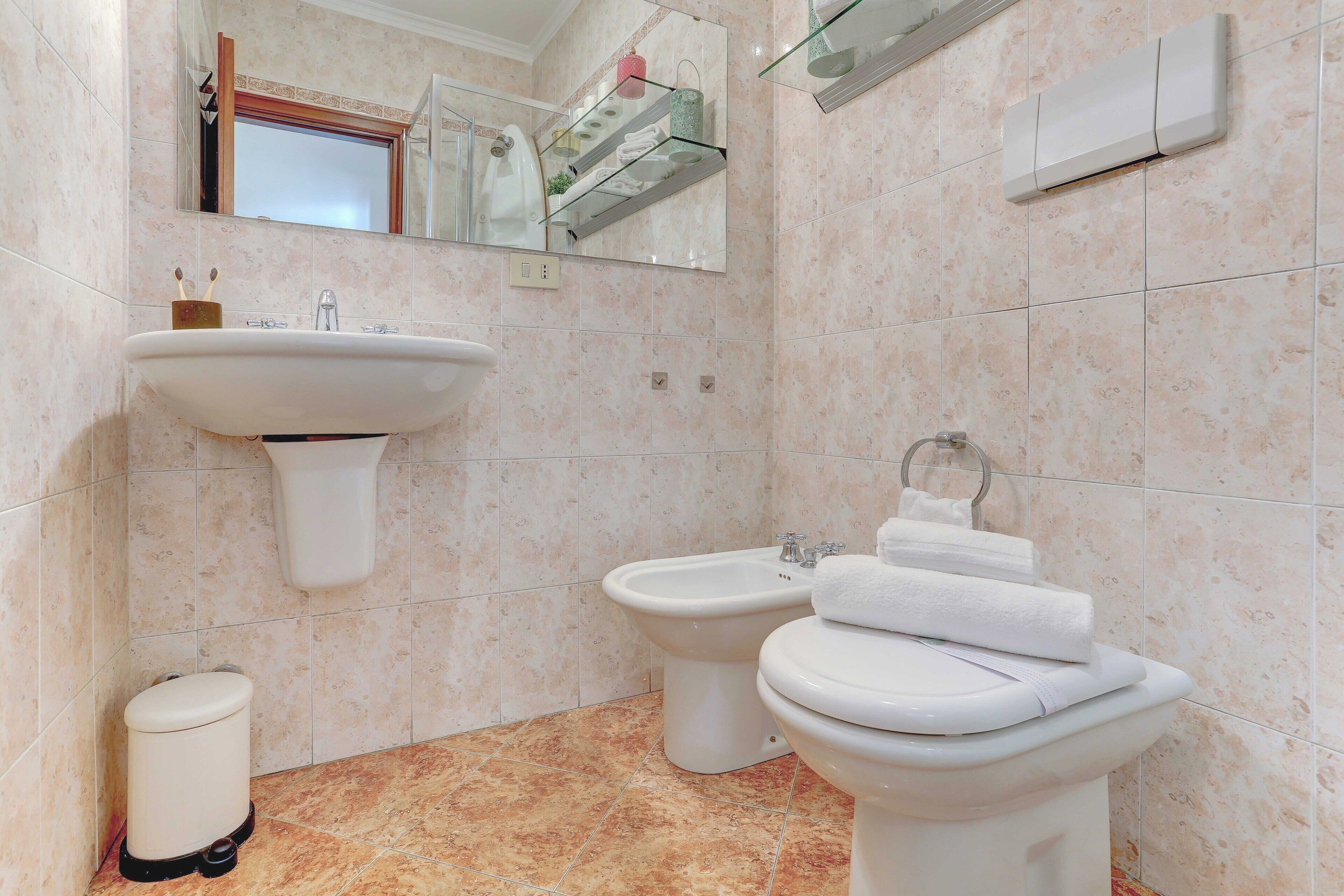 Een badkamer met een wastafel op voetstuk, een toiletbrons, een toilet en een spiegel boven de wastafel.