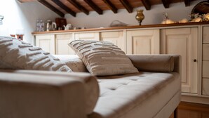 Ein Sofa mit Kissen, eine Holzbalkendecke und im Hintergrund eine Küchenzeile.