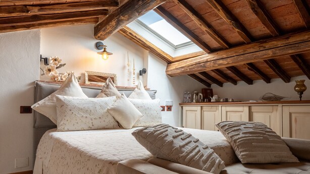 Ein Schlafzimmer mit einem Bett, Kissen, einem Nachttisch, einer Lampe und einem Dachfenster.