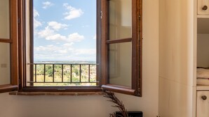 Ein Zimmer mit Fenster und Balkonblick auf den Himmel und entfernte Gebäude.