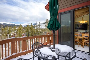 A balcony with a view of snow-covered mountains, a wooden deck, and a table with chairs. - Cloudline Chalet 3 Bedroom Townhouse (Winter Park)