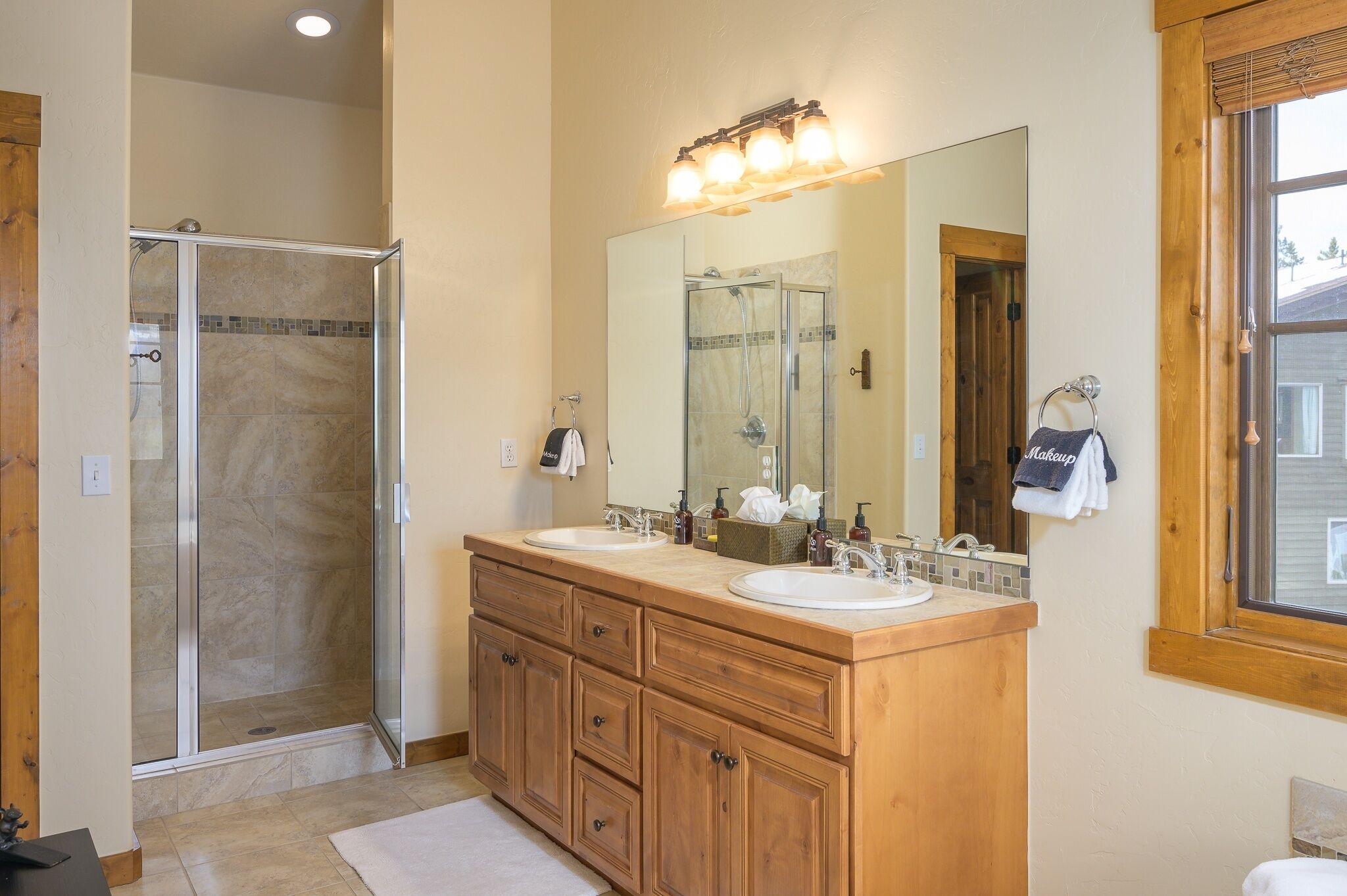 A bathroom with a glass shower enclosure, wooden vanity with two sinks, and a large mirror above the vanity.