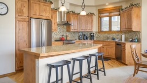 A kitchen with wooden cabinets, a stainless steel refrigerator, a large island with stools, and hanging pendant lights. - Cloudline Chalet 3 Bedroom Townhouse (Winter Park)
