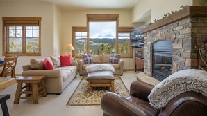 A cozy living room with a fireplace, large windows, and a view of the mountains. - Cloudline Chalet 3 Bedroom Townhouse (Winter Park)