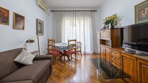 Un salon avec un canapé marron, une table basse en verre, des meubles en bois, un téléviseur et un coin repas comprenant une table et des chaises.